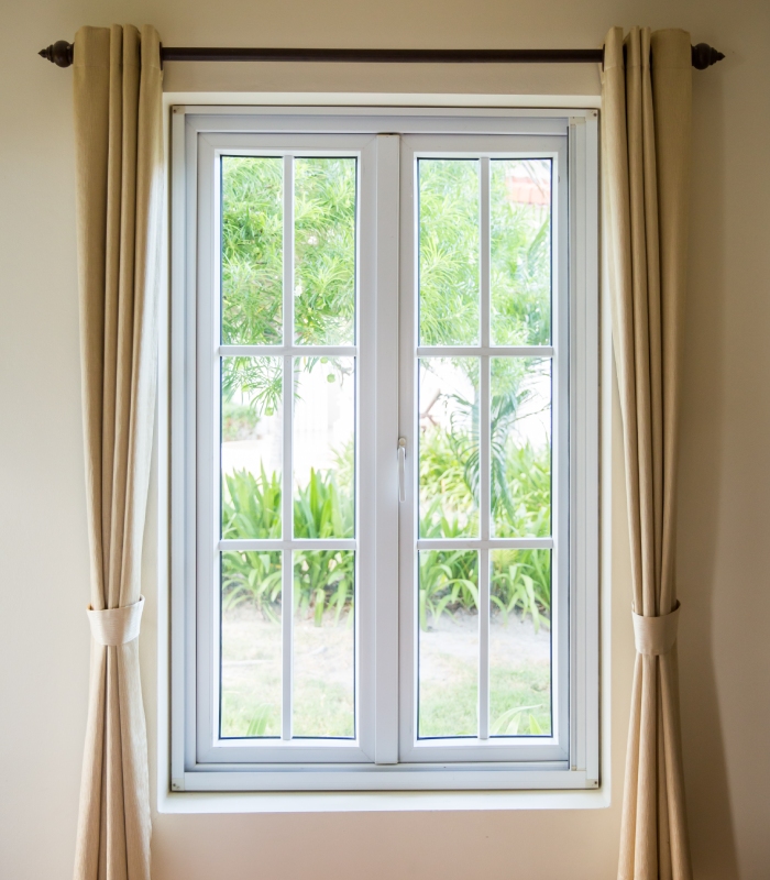 Fenêtre blanche à petits carreaux avec rideaux beiges dans un intérieur lumineux